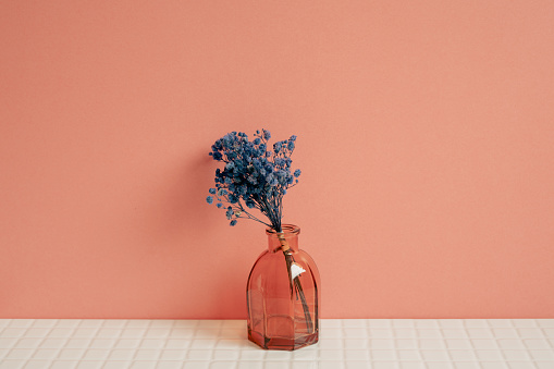 Glass vase of blue gypsophila flowers on white table. pink wall background. home decor