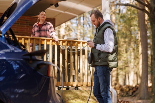 istock Friends plugging the adapter from an electric car to a home power outlet using electrical extension cord to charge it. 1469990393