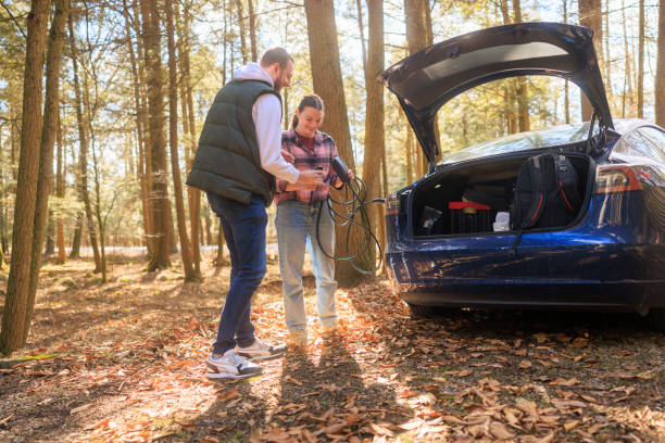 istock Two smiling friends unplugging an electric car adapter from the socket, after charging. 1469990578