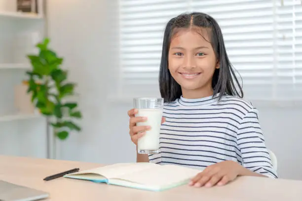 Photo of children women drink milk to nourish the body and nourish the brain. asian young little girl learn at home. girl happy drink milk and read a book for exam, Homeschool. education, vitamins, development