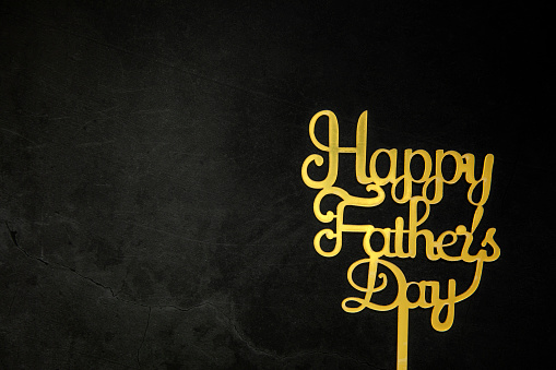 Happy Fathers Day concept. Gold shiny Letters with text Happy Father's Day on concrete dark black background Flat lay, top view, copy space king crown