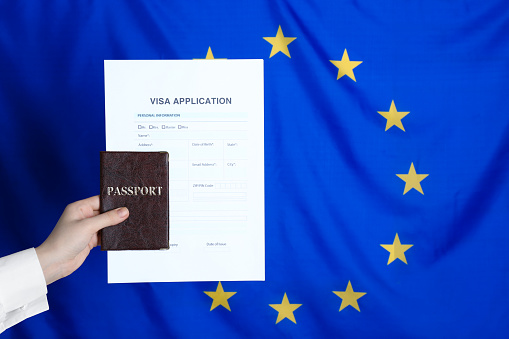Woman holding visa application form and passport against European Union flag, closeup. Space for text