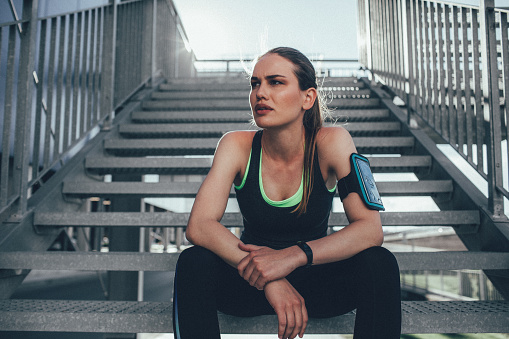 Portrait of Athletic woman after jogging sitting on the staircases. Sportswoman ready to jogging. Woman doing workout outdoor in the city. Sexy fit woman in sports clothes resting and looking away