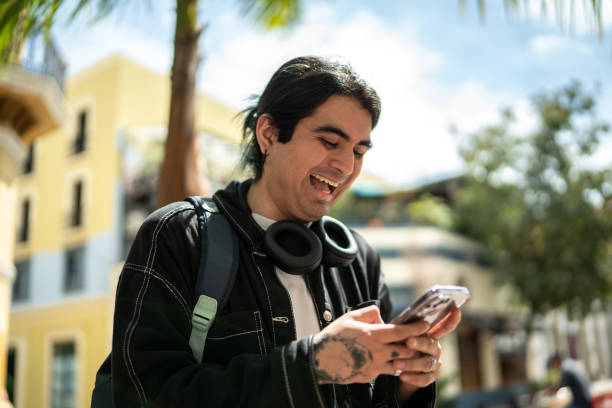 Young man laughing while using a mobile phone at street