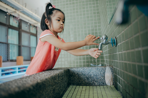 The Asian girl walked up to the school's hand-washing station and thoroughly washed her hands, following the proper steps for hand hygiene to maintain her own cleanliness and health.