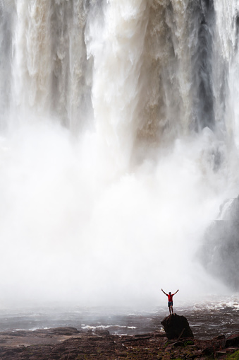 Man gesturing while standing on rock in front of Aponwao fall, La Gran Sabana, Venezuela.