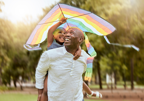 Father, child and rainbow kite outdoor at a nature park for fun, bonding and trust of life insurance and savings of a black family having fun. Black man giving girl piggy back ride on vacation