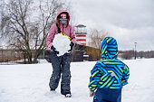 Woman with little boy building a snowman. Family outdoors leisure activity