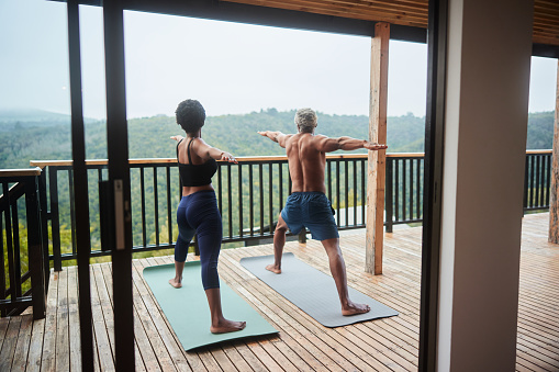 Rear view of a couple practicing the warrior pose during a yoga session together on their balcony with a scenic view