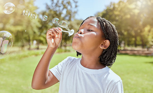 Park, child and black girl blowing bubbles enjoying fun time alone outdoors, joy and childhood development. Happy, freedom and kid learning and playing with soap bubble toy or wand and relax on grass