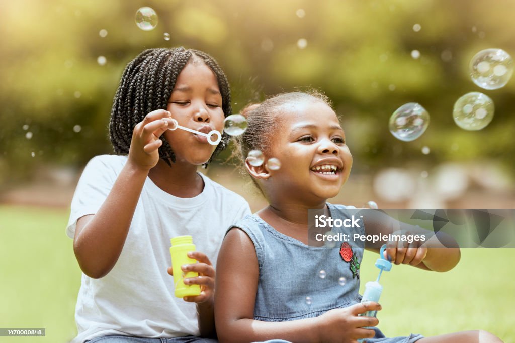 Black kids, children and blowing bubbles at park, having fun and bonding. Girls, happy sisters and playing with soap bubble toys, relax and enjoying garden together outdoors in nature on grass Black kids, children and blowing bubbles at park, having fun and bonding. Girls, happy sisters and playing with soap bubble toys, relax and enjoying quality time together outdoors in nature on grass Child Stock Photo