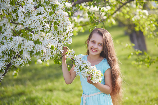 Portrait of a happy little girl with blond curly hair and in a dress. The child enjoys a walk in the botanical park.