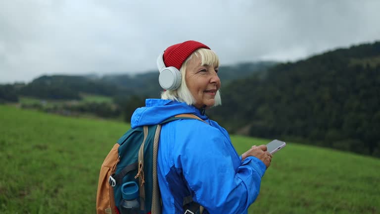 Happy senior hiking woman with headphones in fun exercise, fitness or workout in countryside mountains. Happy, face and comic athlete listening to music, radio or funny audio podcast in nature