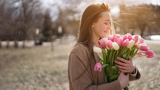 Beautiful girl with tulip flowers in her hands walks in the park