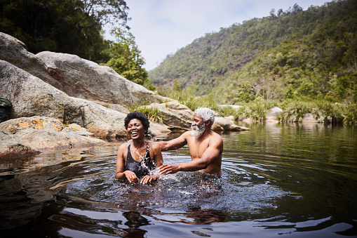 Couple in swimwear laughing while splashing each other during a swim together in a lake in some hills in summer