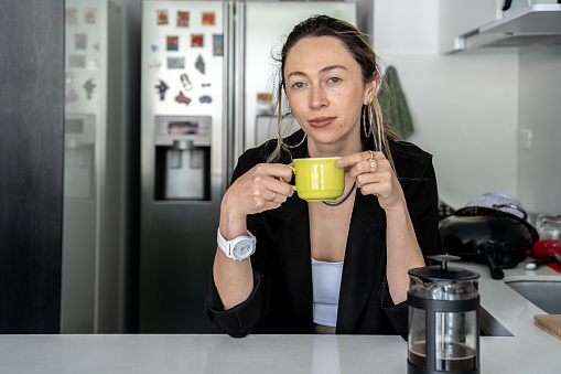 Portrait of a mid adult woman holding a cup of coffee/tea on the kitchen at home