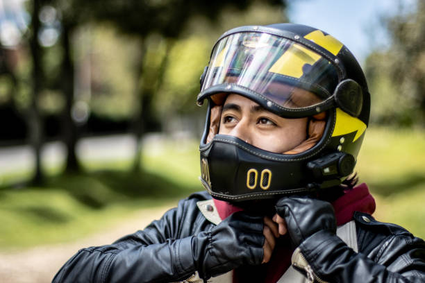 female motorcyclist in a helmet and motorcycle jacket against a white wall