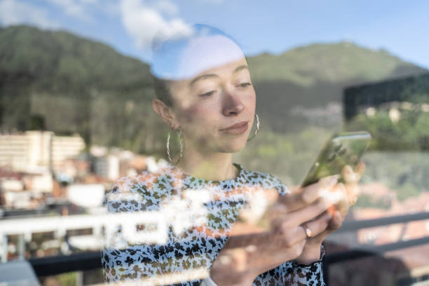istock Mid adult woman using a mobile phone at home - view through window 1470011719