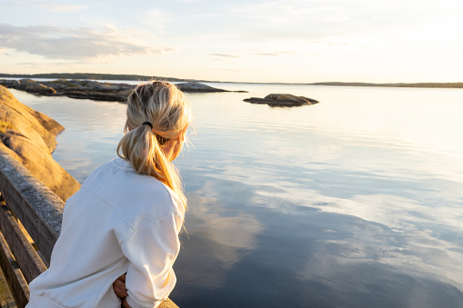 Female standing on wooden bridge between rocky isles and looking at the beauty in nature contemplating peacefulness