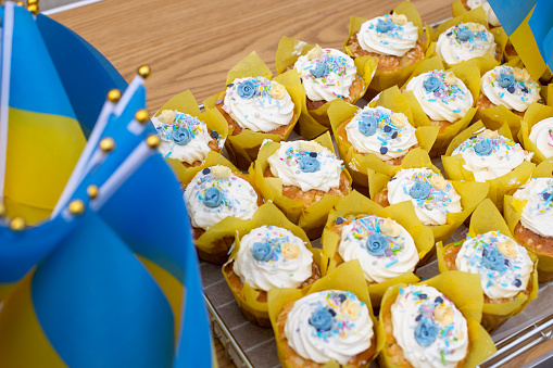 Close up shot of blue and yellow Ukraine themed cupcakes being sold for charity in Polperro, Cornwall. There are Ukrainian mini flags set up beside the cakes.
