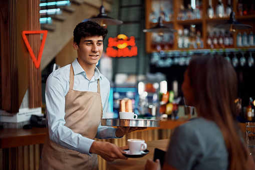 Waiter talking to his customer while serving her coffee in a cafe.