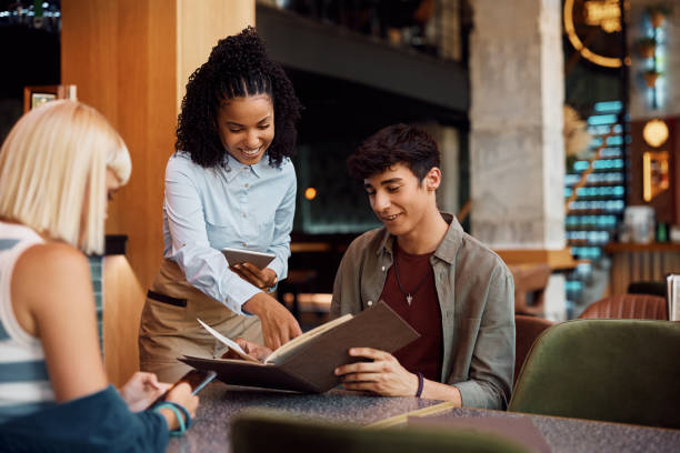 istock Happy black waitress recommending order from a menu to her customers in a cafe. 1470018270