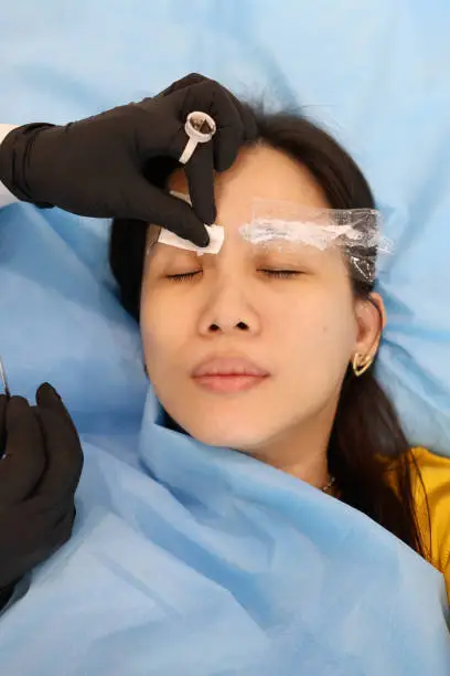 An eyebrow embroiderer is putting anesthetic on a lady's eyebrows.