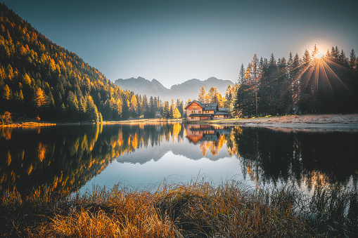 Gorgeous autumn landscape view from Alpine Lake Nambino with colorful pine tree forest background and small cottage, near Madonna di Campiglio. Province of Trento, Trentino Alto Adige, Dolomites, northern Italy.
