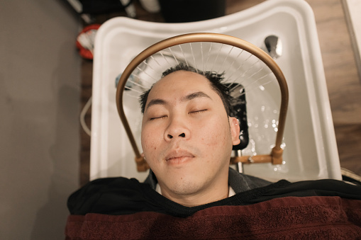 An Asian man is enjoying his hair spa in a hair salon.