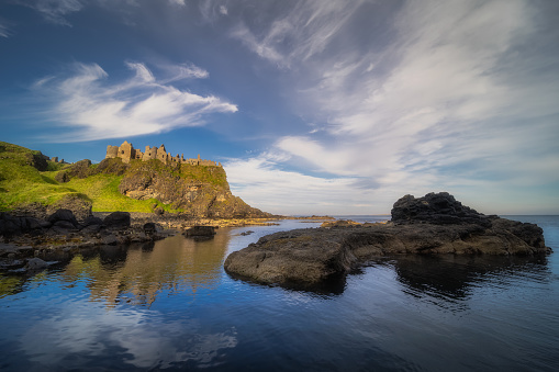 Dunluce Castle reflected in ocean, nested on the edge of cliff, part of Wild Atlantic Way, Northern Ireland. Filming location of popular TV show