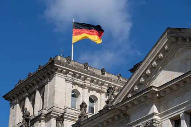 National flag of Germany in the wind and Reichstag building architectural details in Berlin, Germany.