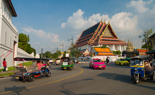 Bangkok, Thailand. December 9, 2022. View of Phu Pha Suthat Fort and The Reclining Buddha shrine. Thai Wang Alley street junction. Tuk tuk taxis and modern taxis are in traffic. Asia travel route.