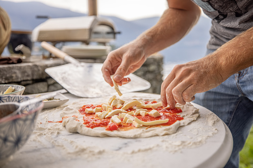 Making Italian pizza at home in the garden using a small domestic wood fire pizza oven, baking fresh pizza with a stunning view of lake Maggiore