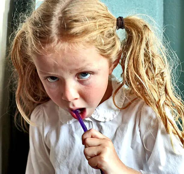 Little girl reluctantly follows the rule to brush her teeth before heading off to school.
