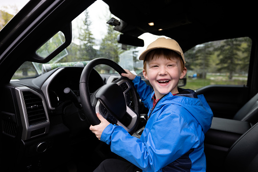 Young 6 years old redhead boy smiling and looking at the camera while being inside a pick-up truck on a road trip in the Canadian Rockies.