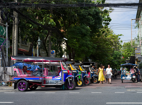 Bangkok, Thailand, December 9, 2022. Traditional tuk tuk taxis and tourists in Ram Buttri street. Street near Chakrabongse road.