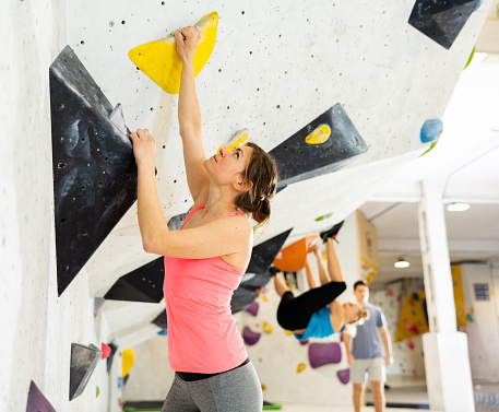 Young female alpinist practicing indoor rock-climbing on a artificial boulder without the safety belts