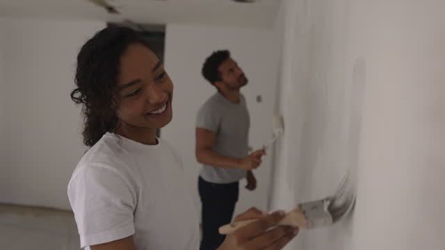 Happy African American couple having fun painting a wall in their house together