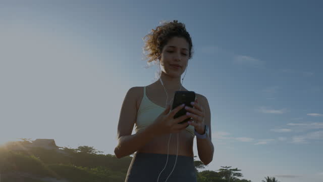 Beautiful woman selecting a playlist on her smartphone before starting her morning jog at the beach