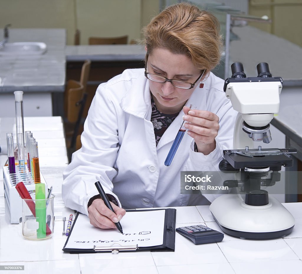 Female scientist holding test tube and taking notes Female researcher taking notices at her workplace.All inscriptions are mine. Adult Stock Photo