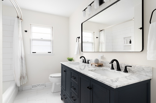 A beautiful bathroom with a dark blue vanity cabinet, marble countertop, and large mirror below a light.