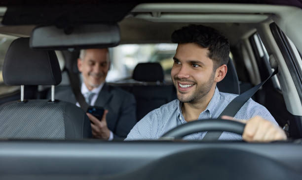 Driver transporting a business man on a crowdsourced taxi Happy Latin American driver transporting a business man on a crowdsourced taxi - transportation concepts taxi driver stock pictures, royalty-free photos & images