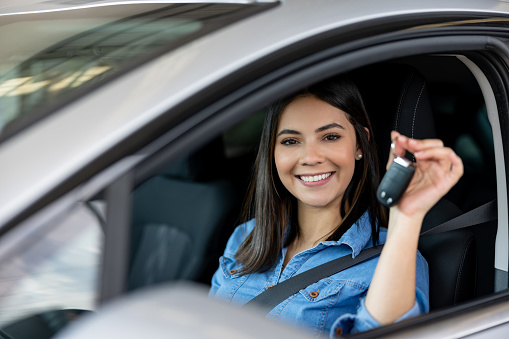 Beautiful Latin American woman looking very happy holding the keys of her new car and smiling at the camera