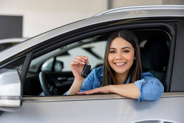 glückliche frau, die die schlüssel ihres neuen autos im autohaus hält - car car rental car dealership key stock-fotos und bilder