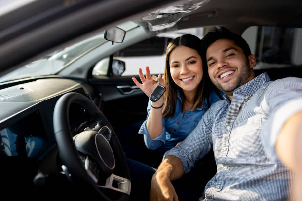 pareja feliz sentada en su nuevo auto y sosteniendo las llaves - new automobile fotografías e imágenes de stock