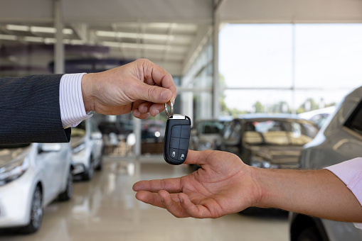 Close-up on a car salesperson giving the keys to a client buying a car at the dealership