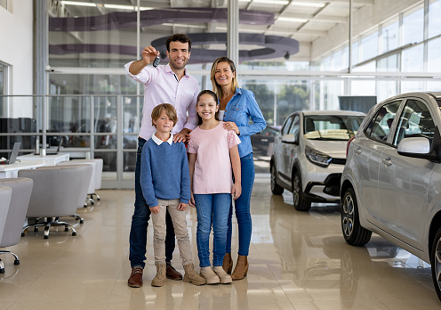 Happy Latin American family holding the keys of their new car at the dealership and looking at the camera smiling
