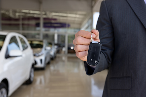 Close-up on a car salesperson holding keys at the dealership - car ownership concepts