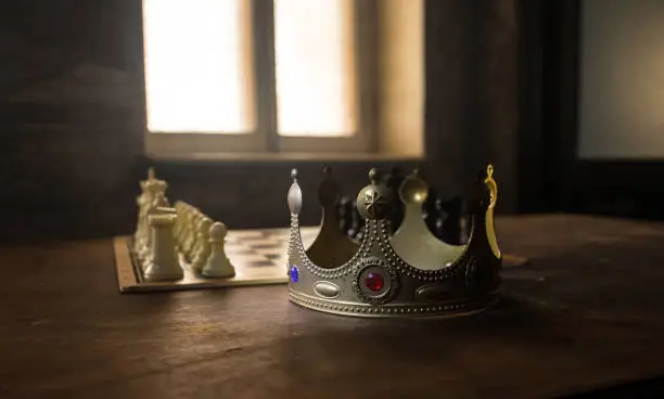 Photo of Beautiful crown miniature on chessboard. chess board game concept of business ideas and competition and strategy ideas concept. Chess figures on a dark background with smoke and fog. Selective focus