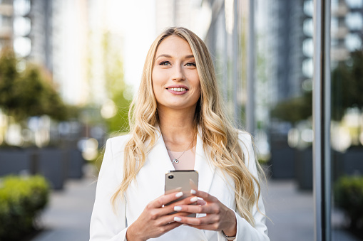 Portrait of a female entrepreneur in a white blazer holding a smart phone. Modern businesswoman.